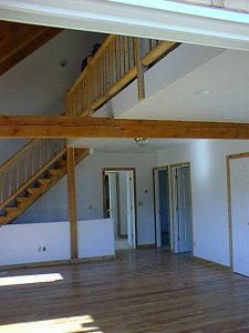 Emty house with loft going across perpendictular to cross beam and stairs at back wall. No furnishings.