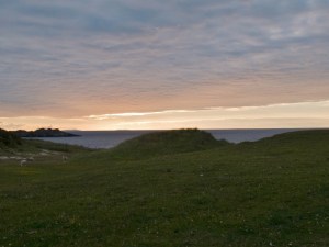 green hill leading to beach with sunrise over small bay