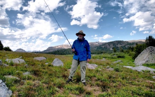 man with fishing pole posed against rocky mountains