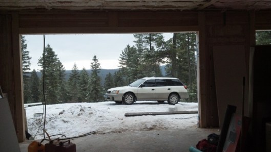looking out a garage under construction with white subaru in snow with mountains behind
