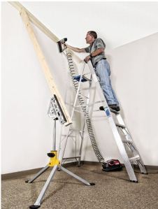 Man standing on ladder nailing ceiling molding with Jawstand holding 2 x 4s that brace the unfastened end of the molding