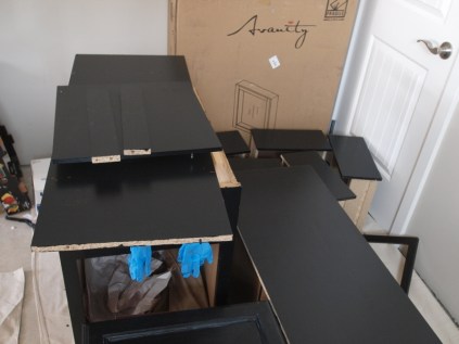 stack of furniture parts painted black with blue latex gloves hanging from the middle