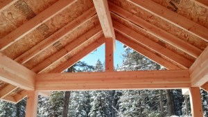 house under construction view thorugh king post of porch looking at evergreens with snow