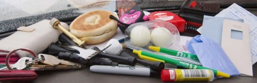 photo of things taken from a woman's purse including white and pink wallet, lipstick, dog poop bag, building supplies and pens