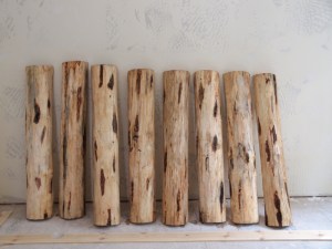 eight half logs that will become stair treads lined up against a dry wall that has been textured but not painted in new construction