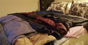 bed covered with coats and vests and a curtain to use for covers