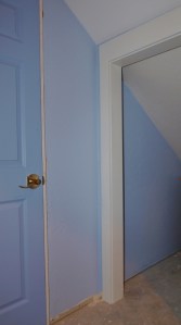sloped wall bisected by door frame. The ceiling is sloped and white, the wall blue. The door frame bisects.
