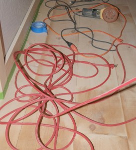 unfinished floor with multiple electrical cords sprawled about, includes an orbital sander