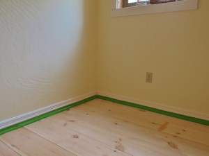 the corner of a room with green masking tape on the floorboards