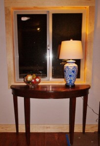 half-round table sitting in front of window with blue china lamp and bowl of fruit on it