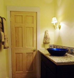 bathroom counter with blue and yellow tile back splash, white pine door, colonial wall light, countertop with blue vessel sink